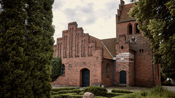 Det er et gammelt teglmurstenshus med spisse tårne og en murstensgård med buske og træer.