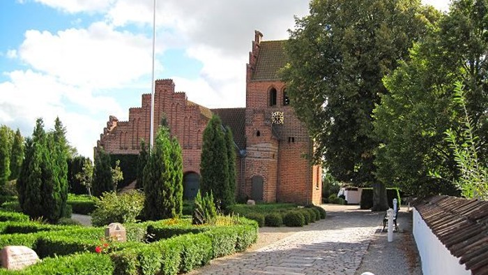 En murstenskirke med tårn og en smuk have med stier og planter