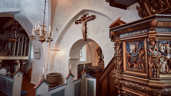 Kirkens indre rum med alter, krucifix og bænke.