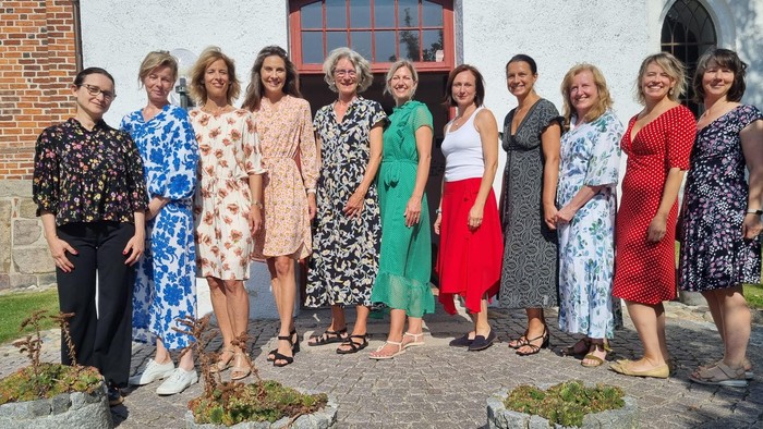 En gruppe af kvinder står sammen udenfor et murstenshus.