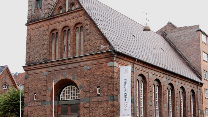 Historisk rødstenskirke med et højt spir og en buet indgang på et gadehjørne i byen.
