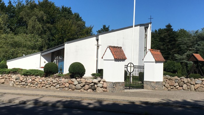 En lille, hvid kirke med røde tag og en mur af sten omkring.