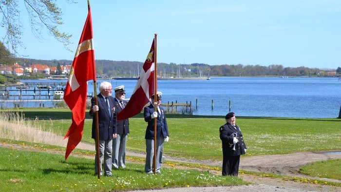 En gruppe personer holder to store flag i en park ved vandet