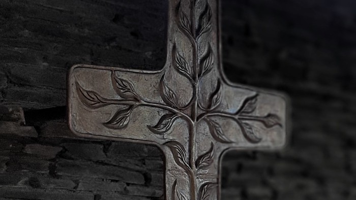 Ein Kreuz mit Baumrelief an einer Ziegelmauer.