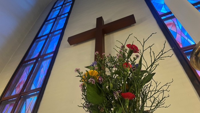 En blomsterstang med røde og gule blomster under et kors på en kirkemur