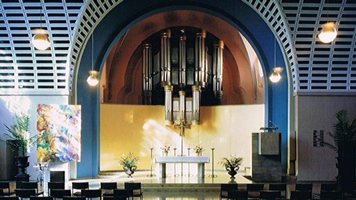 Elegantes Kircheninneres mit einer prächtigen Pfeifenorgel, Altar, Buntglasfenstern und warmem Licht.