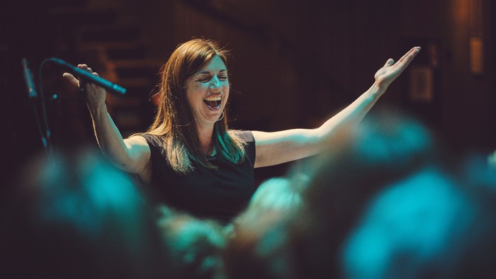 Lidenskabelig performer på scenen med udstrakte arme, der synger ind i en mikrofon under farverigt lys.