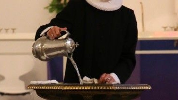 Præst hælder vand op i døbefont