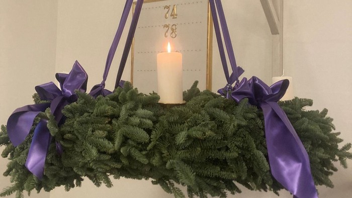 en grøn krans med lilla bånd og et tændt lys