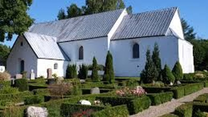 Et smukkt hvidt kirkebygning med en velholdt have og træer.