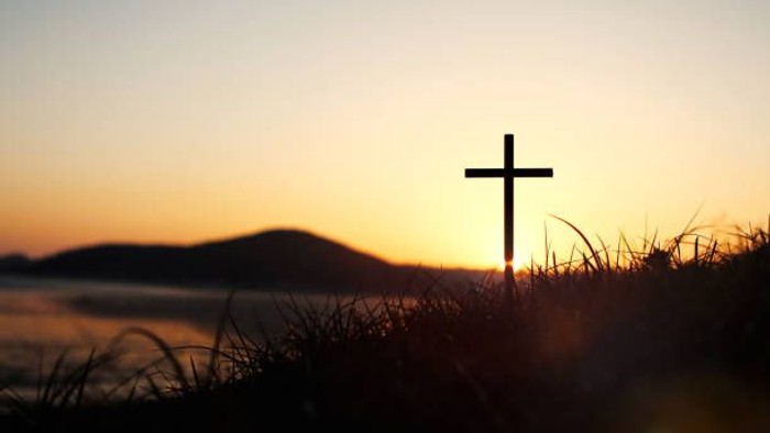 Ein Kreuz vor Sonnenuntergang mit Bergen und Wasser im Hintergrund