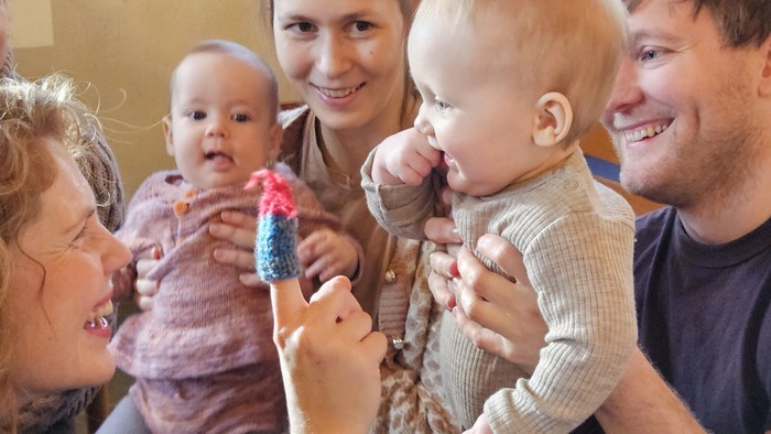En glad gruppe voksne og babyer, der glædeligt leger indendørs med farverige legetøj.