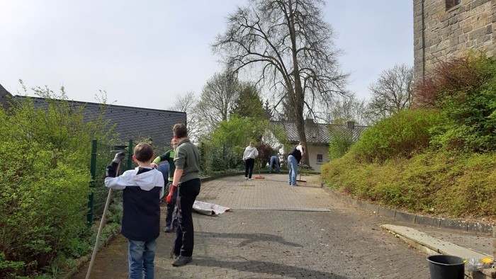 Einige Menschen gehen auf einem Feldweg, einer hält einen Stock, andere tragen Taschen.