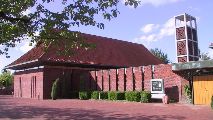 En rød murstenskirke med tårn og træer foran