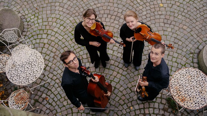 Et kvartet af musikere, der spiller på strygeinstrumenter i en mønstret udendørs gård.