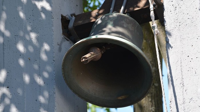 Eine Glocke ist an der weißen Wand befestigt.