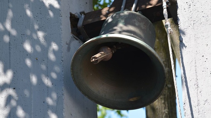 Eine Glocke ist an der weißen Wand befestigt.