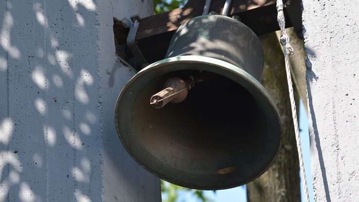 Eine Glocke ist an der weißen Wand befestigt.