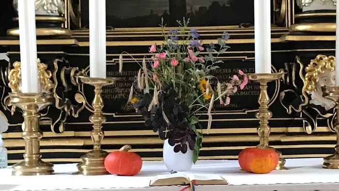 Elegant alteropsætning med lys, blomster, æbler og prægtige religiøse dekorationer på et overdækket bord.