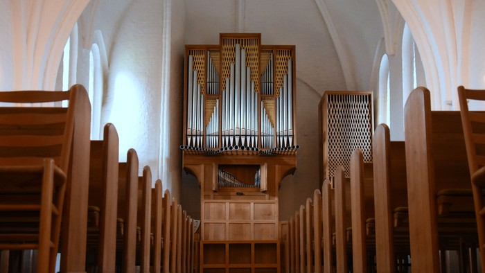 Indenrigspart af kirke med orgel og træbænke.