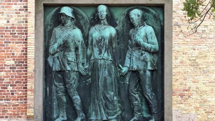 Støvletøg med tre figurer foran murstengevær