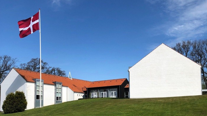 Hvidt hus med rødt tag og dansk flag på en bakke