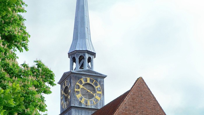 Kirketårn med klokke og spire mod en blå sky