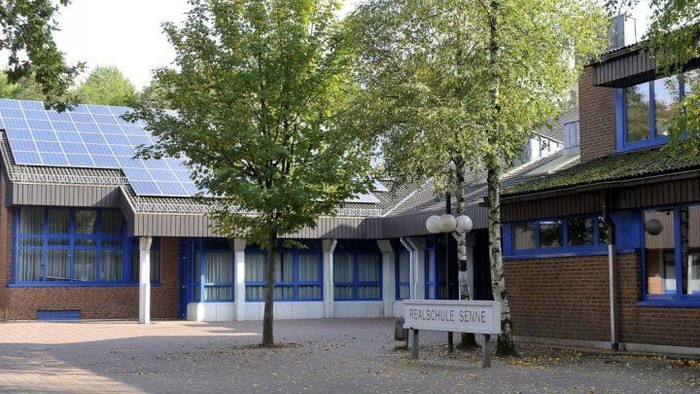 Modernes Schulgebäude mit Solarpaneelen, umgeben von Bäumen und beschriftet mit „Realschule Sennie“.