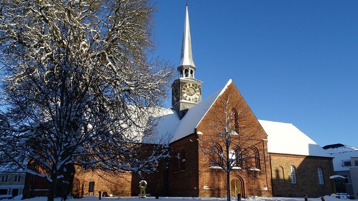 En snede kirke med klokketårn og en især snebelagt træ foran