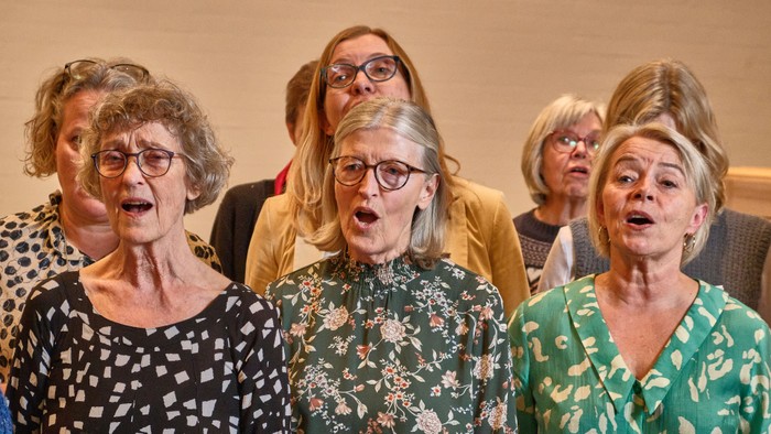 Gruppe af ældre kvinder, der glædesfyldt synger sammen med åbne munde og udtryksfulde ansigter.