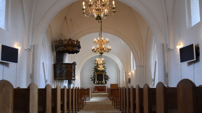 Indre del af kirke med høje vægge og belysning fra kandelier
