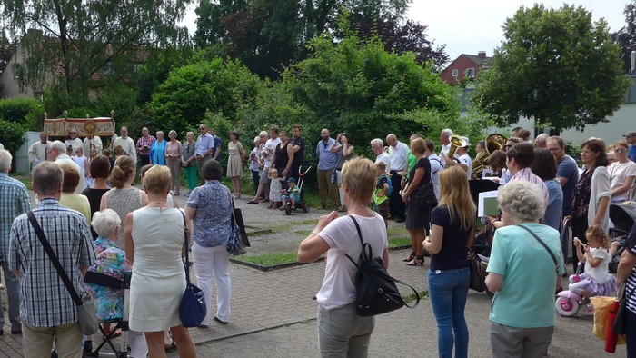 Eine Gruppe von Menschen versammelt sich im Freien, einige mit Kinderwagen, vor einem Haus.