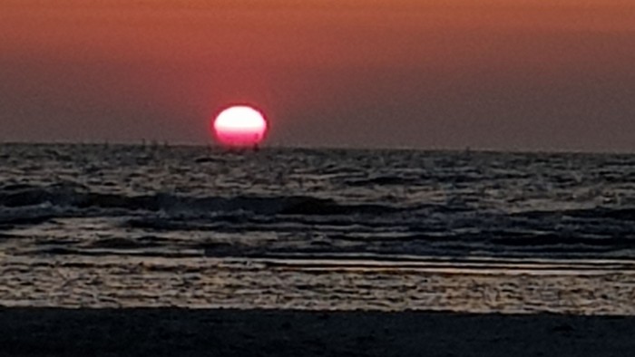 Solnedgang over havet med en levende rød-orange himmel og en delvist skjult sol.