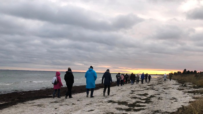 En gruppe af mennesker går på en strand ved solnedgang