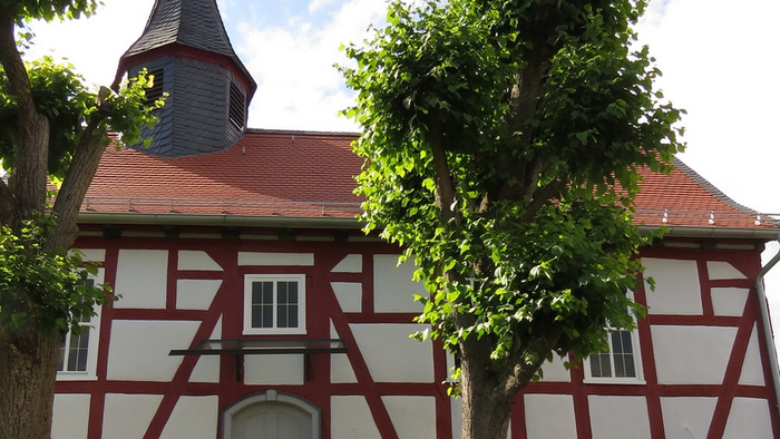 Das Bild zeigt ein traditionelles deutsches Fachwerkhaus mit einem spitzen Dach und einem Wetterhahn.