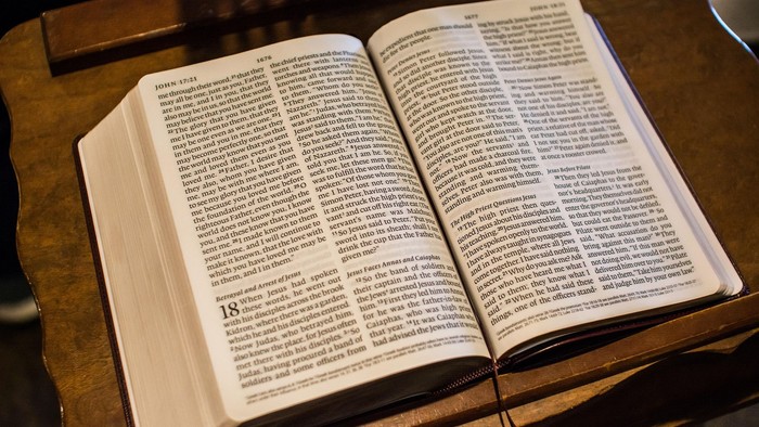 Geöffnete Bibel mit Text auf beiden Seiten, liegend auf einer Holzfläche.