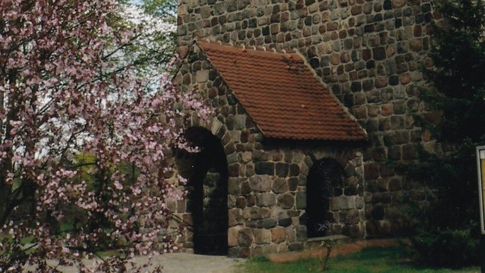 Eingang der Dorfkirche mit blühendem Strauch auf der linken Seite des Bildes