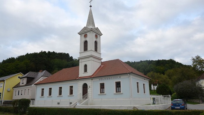 Kleine Kirche mit Uhrturm und rotem Dach in ländlicher Umgebung