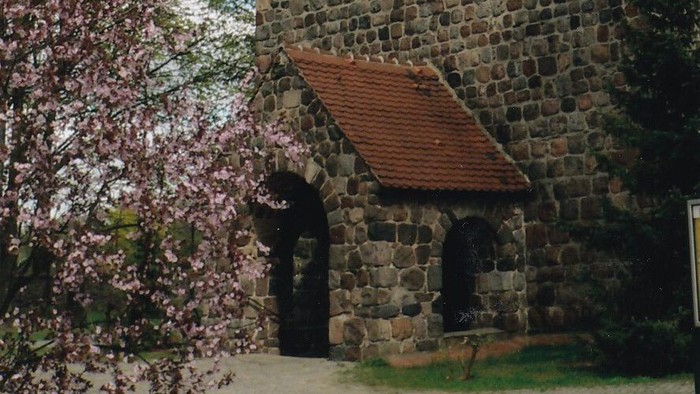 Eingang der Dorfkirche mit blühendem Strauch auf der linken Seite des Bildes