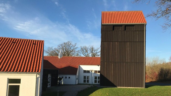 En moderne bygning med rød tag og en høj, træklædt tårn ved siden af en hvid bygning med rød tag og græsplæne foran