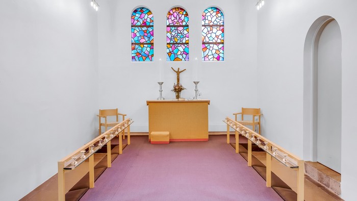 En lille kapel med farverige vinduesglas, alter med krucifix og tre stolene foran