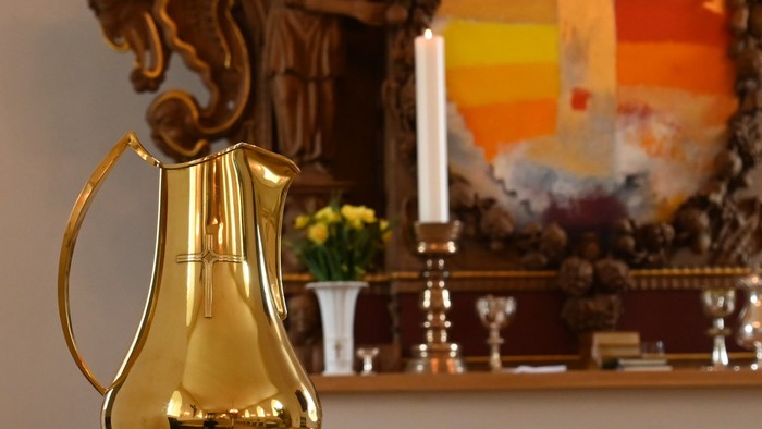 Gylden kande på bord foran religiøs kunst