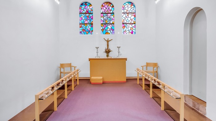 En lille kapel med farverige vinduesglas, alter med krucifix og tre stolene foran