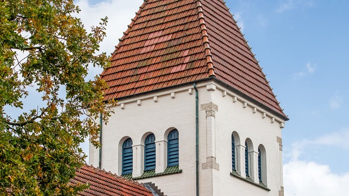 Hvid kirke med røde tag og tårn med kors.