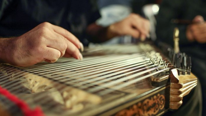 Un musicien joue d'un guzheng traditionnel, une cithare chinoise, en posant ses mains concentrées sur ses cordes.