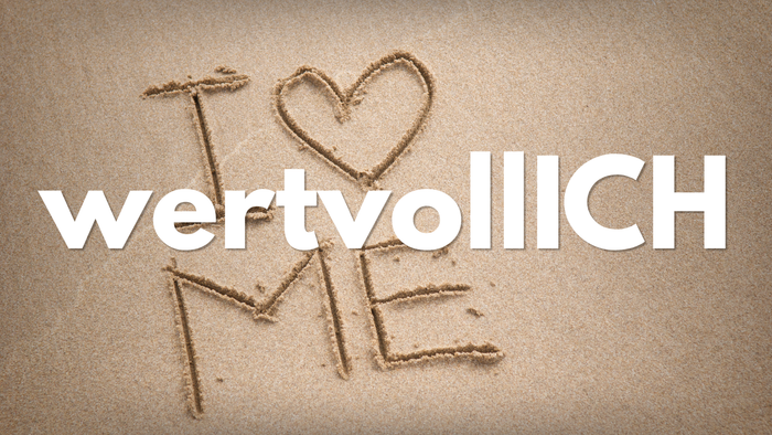 Herzförmige Botschaft „wertvoll“ mit „ICH“ in den Sand geritzt, die den Selbstwert am Strand betont.