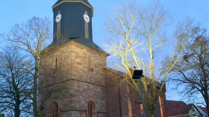 Kirchturm mit Uhr und spitzen Dach bei Dämmerung