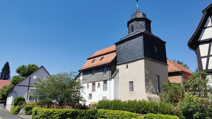 Ein weißes Gebäude mit schwarzem Dach und Uhrturm, umgeben von grünen Büschen und Bäumen