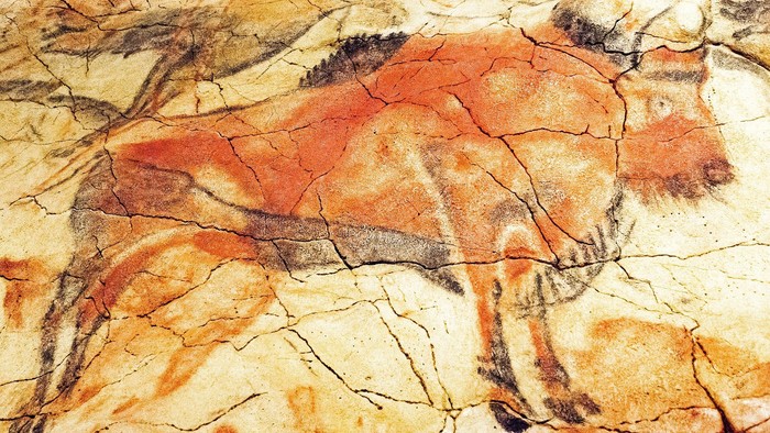 Gammelt hulemaleri, der afbilder en stiliseret dyrefigur med rødlige og sorte pigmenter på en ru klippeoverflade.