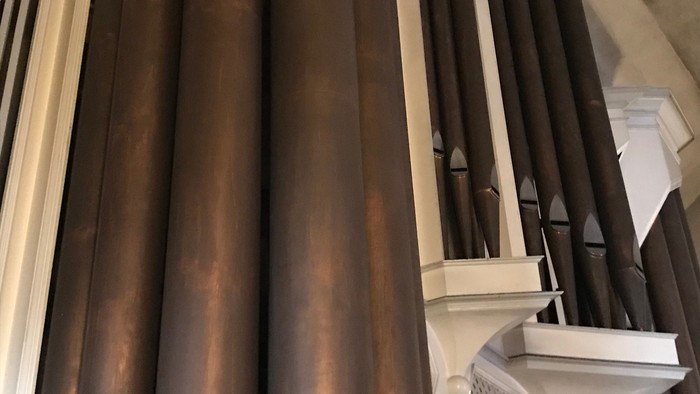 Nahaufnahme polierter kupferfarbener Orgelpfeifen in einem klassischen architektonischen Ambiente.